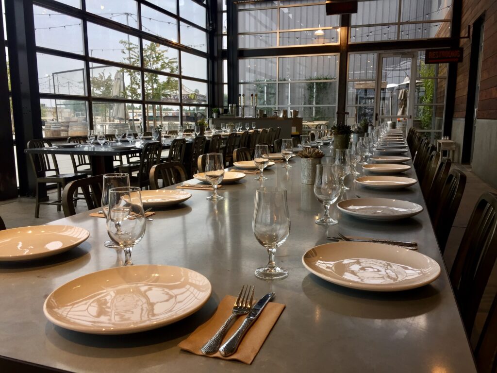 Multiple plates, eating utensil, and glass nicely setup on a long table for an upcoming event.