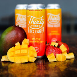 Picture of Thirty Three Seltzer Strawberry Mango can with fresh cut mangoes and strawberries