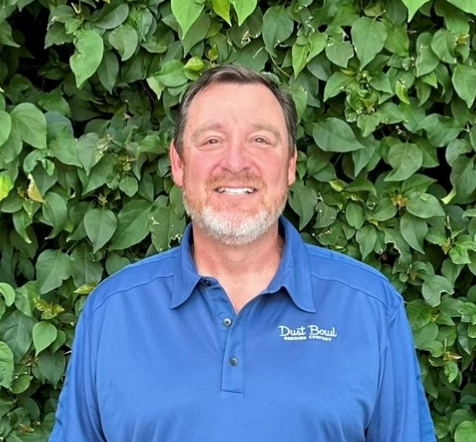 Picture of Kevin Riddiough in front of a leaf background with a blue Dust Bowl polo